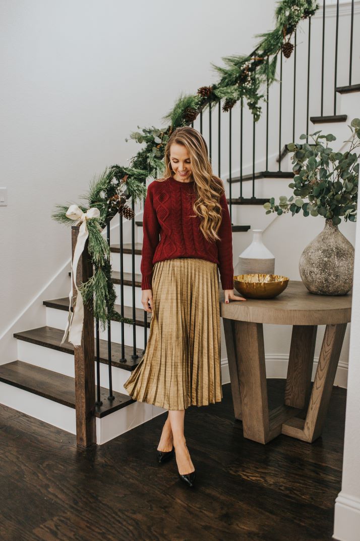 gold pleated skirt and burgundy cable knit sweater in front of curved staircase and round entry table